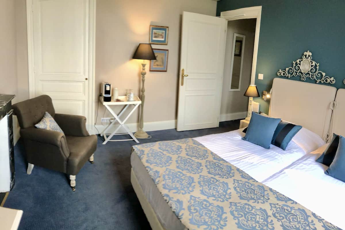 A hotel room with a bed, a chair, a desk, a lamp, and a mirror.