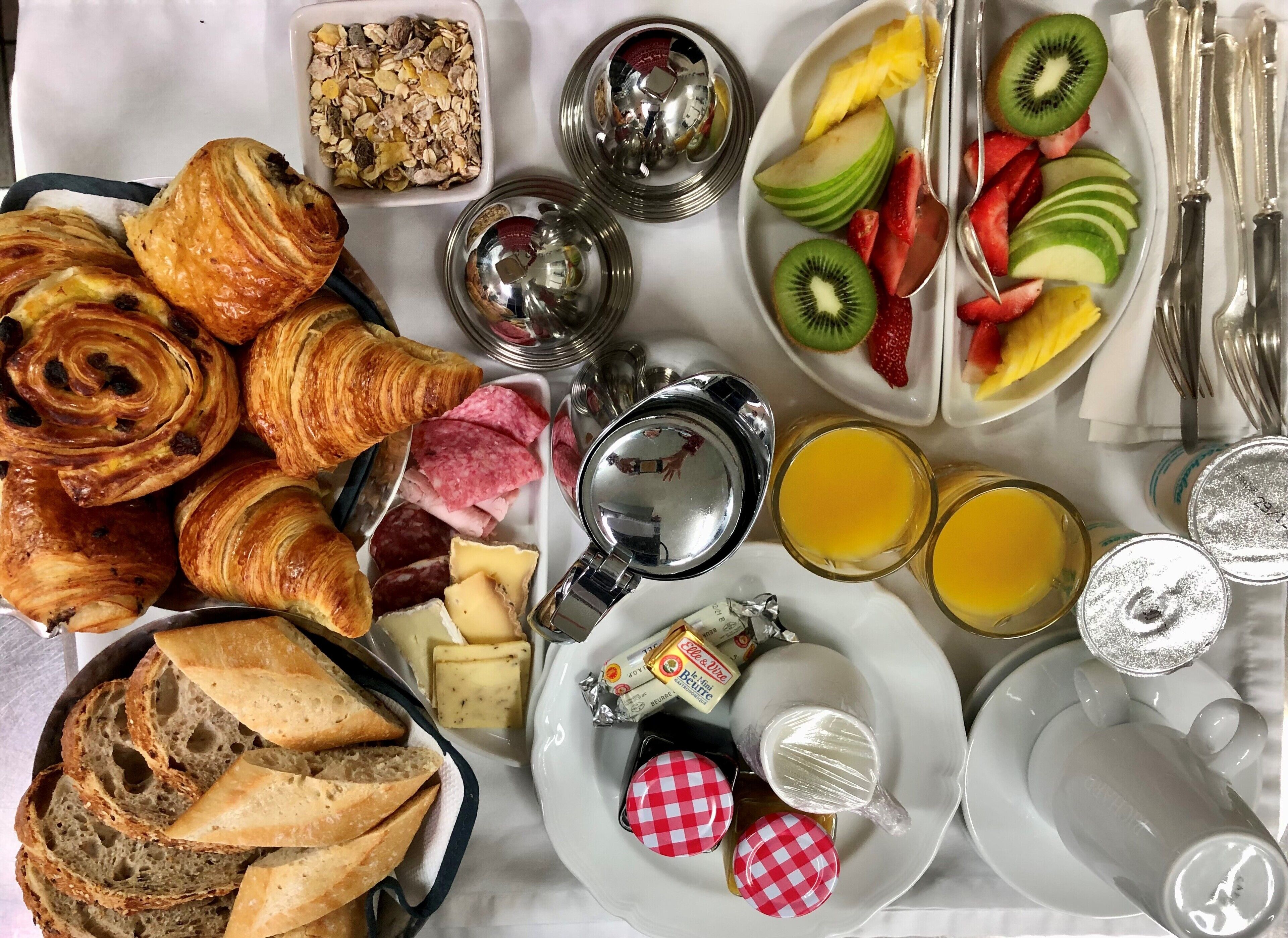 A breakfast spread with pastries, cheese, fruits, and beverages on a table.