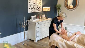 Une salle de spa équipée d’une table de massage, d’une commode blanche agrémentée d’objets décoratifs, d’un miroir et d’un mur orné de motifs complexes.