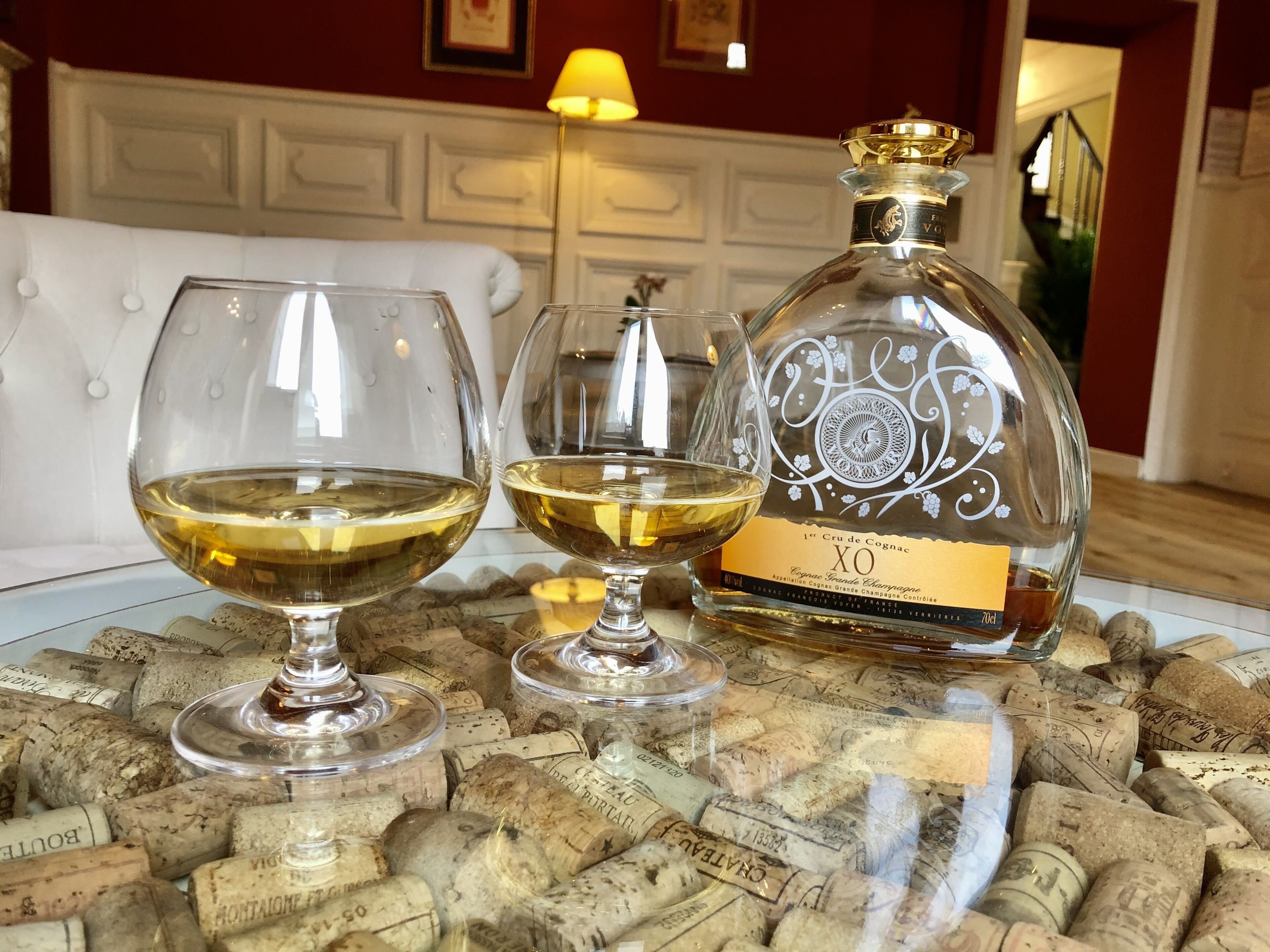 A bottle of XO Cognac and two glasses on a table covered with wine corks.