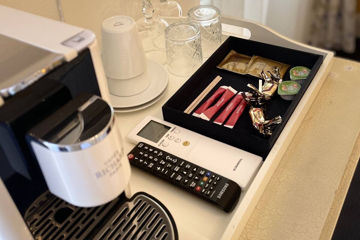 A hotel minibar with a coffee machine, a remote control, and a tray with snacks and glasses.