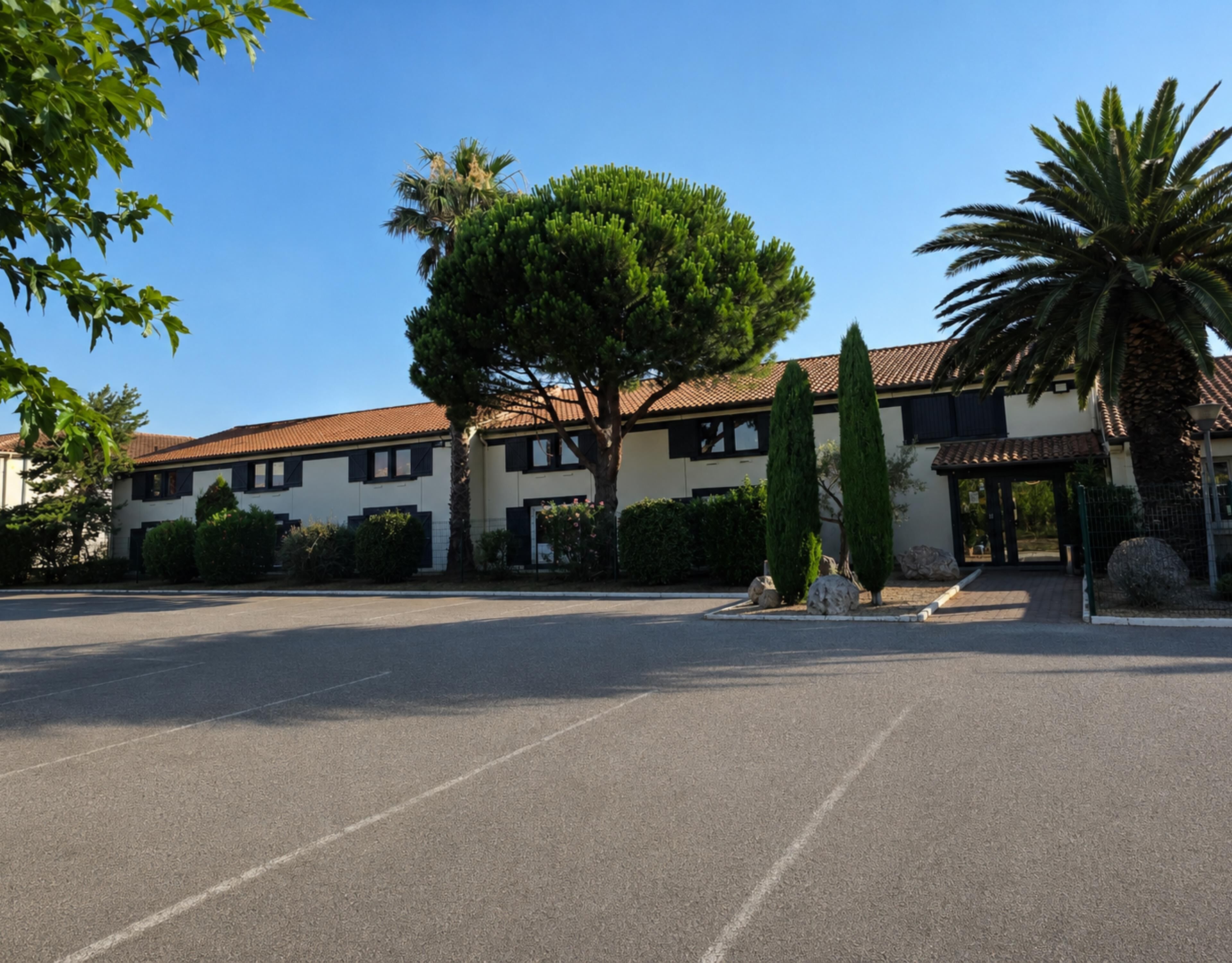 A building with a parking lot, a covered entrance, and a palm tree.