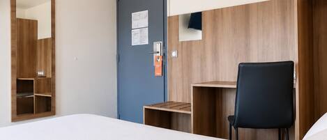 Una habitación de hotel con cama, escritorio, silla, armario y puerta.