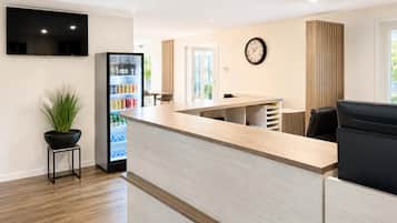 Un espace d’accueil comprenant un comptoir, un téléviseur fixé au mur, une horloge et un réfrigérateur rempli de boissons.
