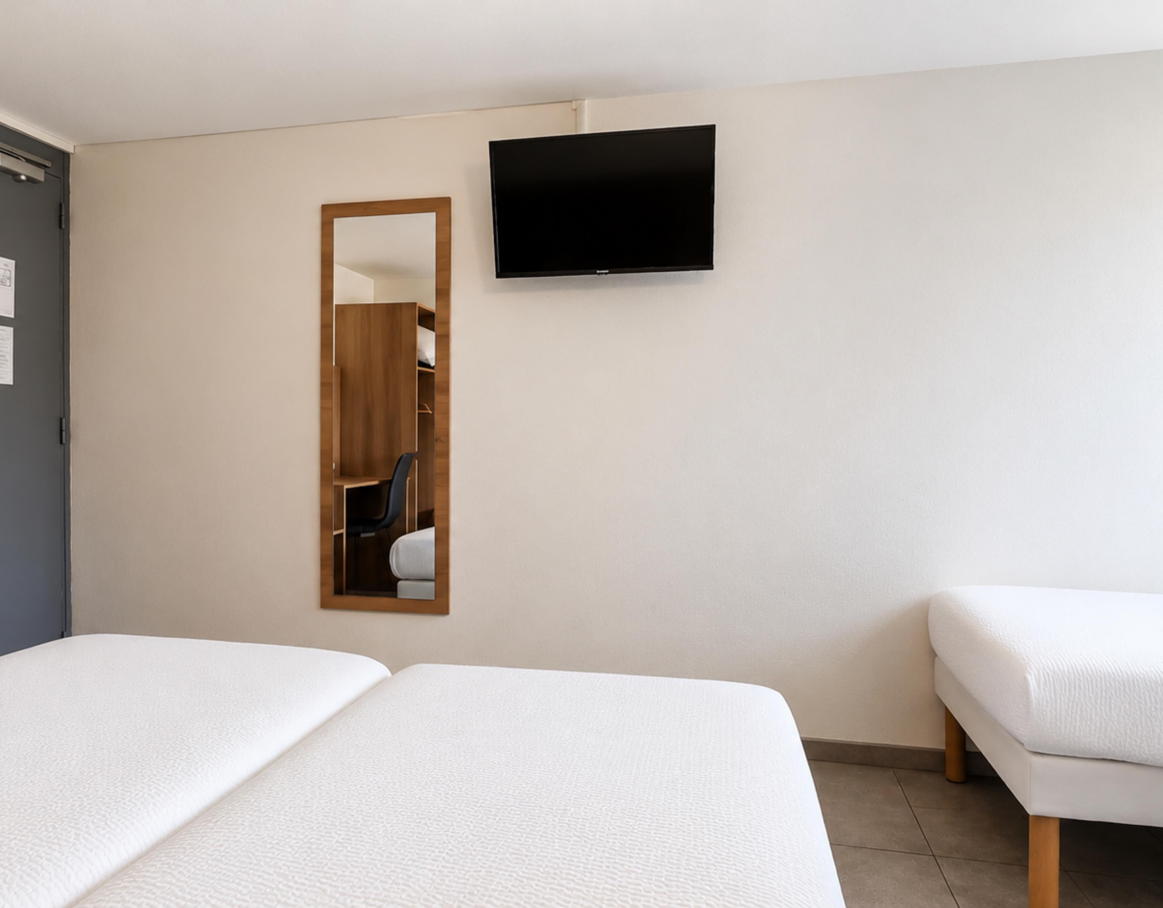 Habitación de hotel con dos camas, un televisor montado en la pared y un espejo que refleja la habitación.