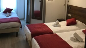 A hotel room with two beds, each with red and white bedding, a mirror, an air conditioning unit, and a window with curtains. - Kyriad - Narbonne Sud (Narbonne)
