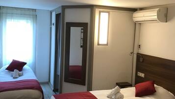 Une chambre d’hôtel avec deux lits, chacun agrémenté de draps rouges et blancs, un miroir, un appareil de climatisation et une fenêtre avec des rideaux.