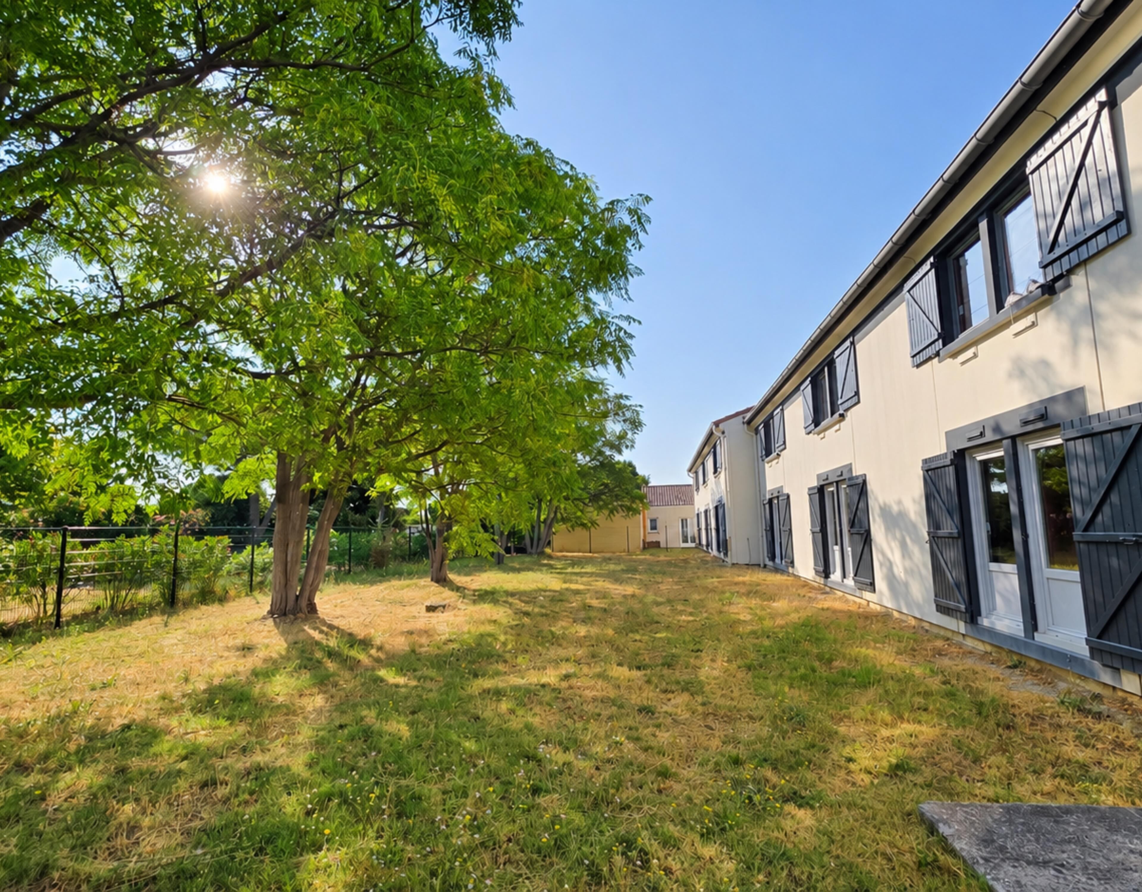 A residential area with a grassy lawn, trees, and a row of houses with shutters.