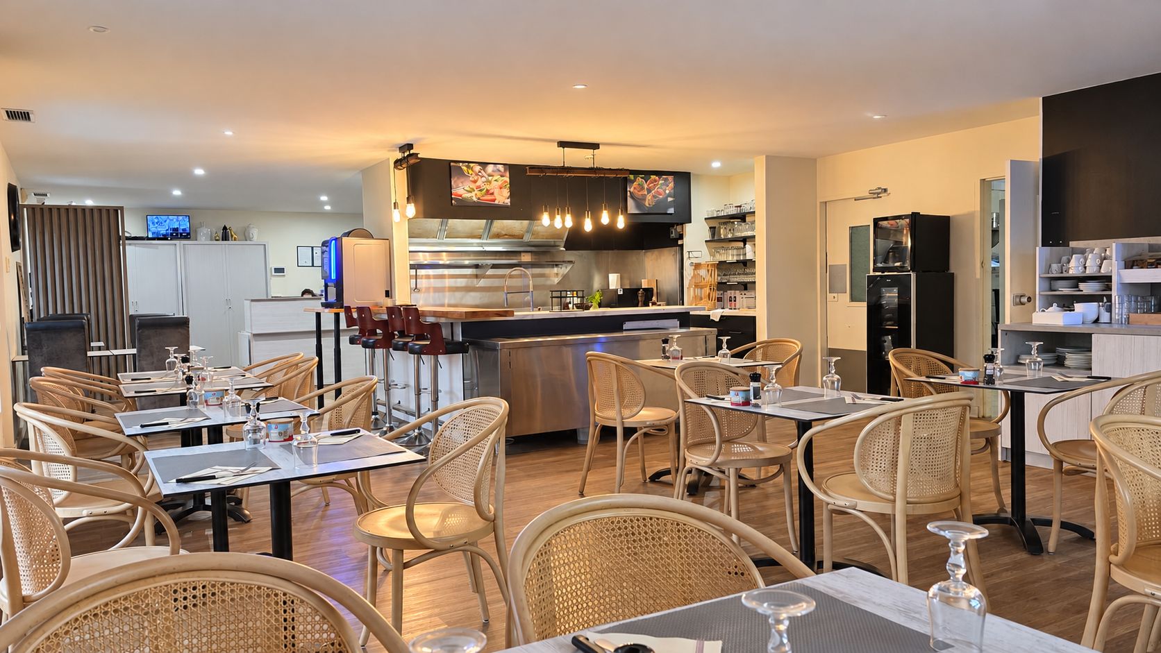 Un restaurant doté de plusieurs tables et chaises, d’un espace cuisine et d’un bar.