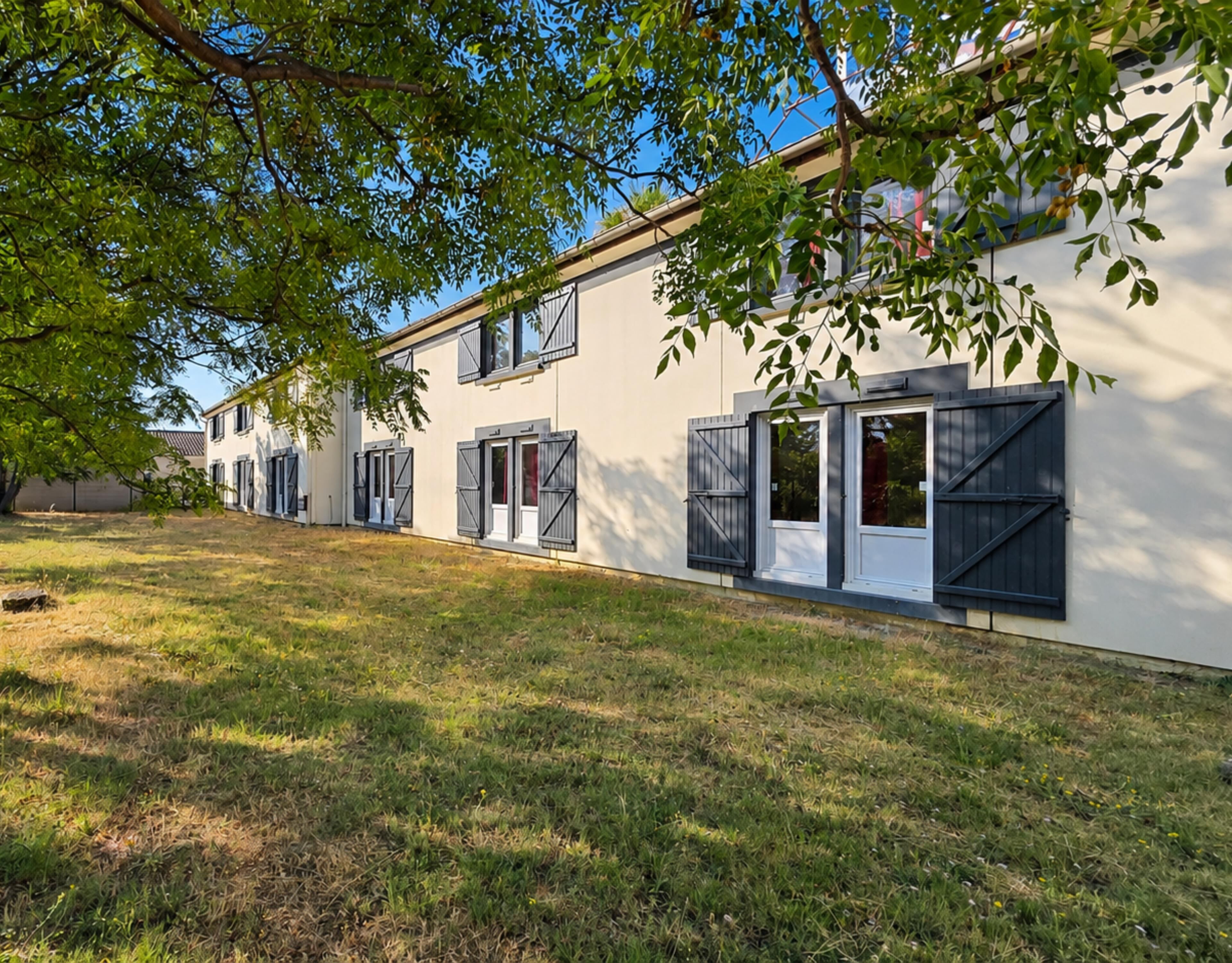 A row of white buildings with black shutters, a grassy lawn, and trees in the foreground.