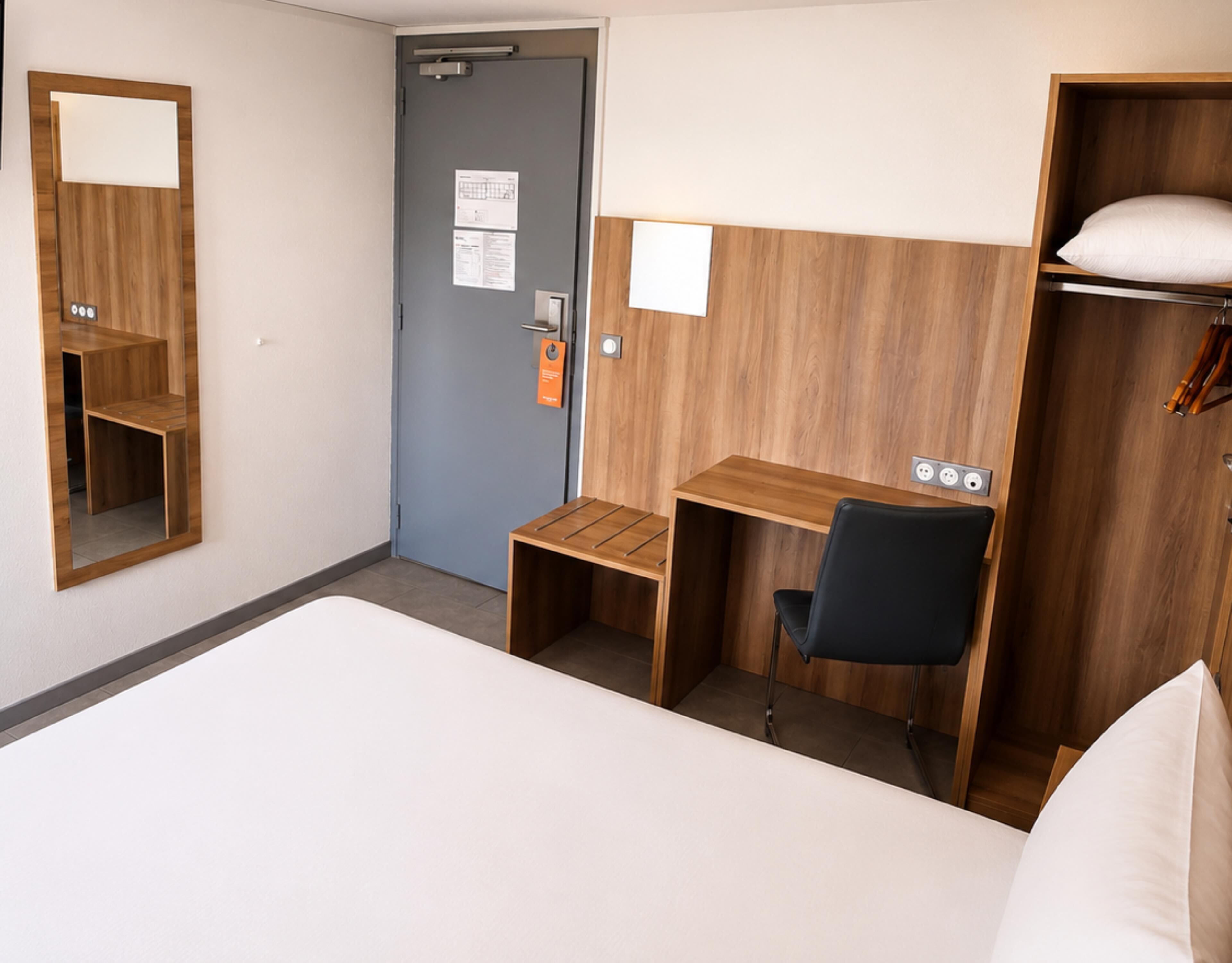 Une chambre d’hôtel avec un lit, un bureau, une chaise, une armoire et une porte.