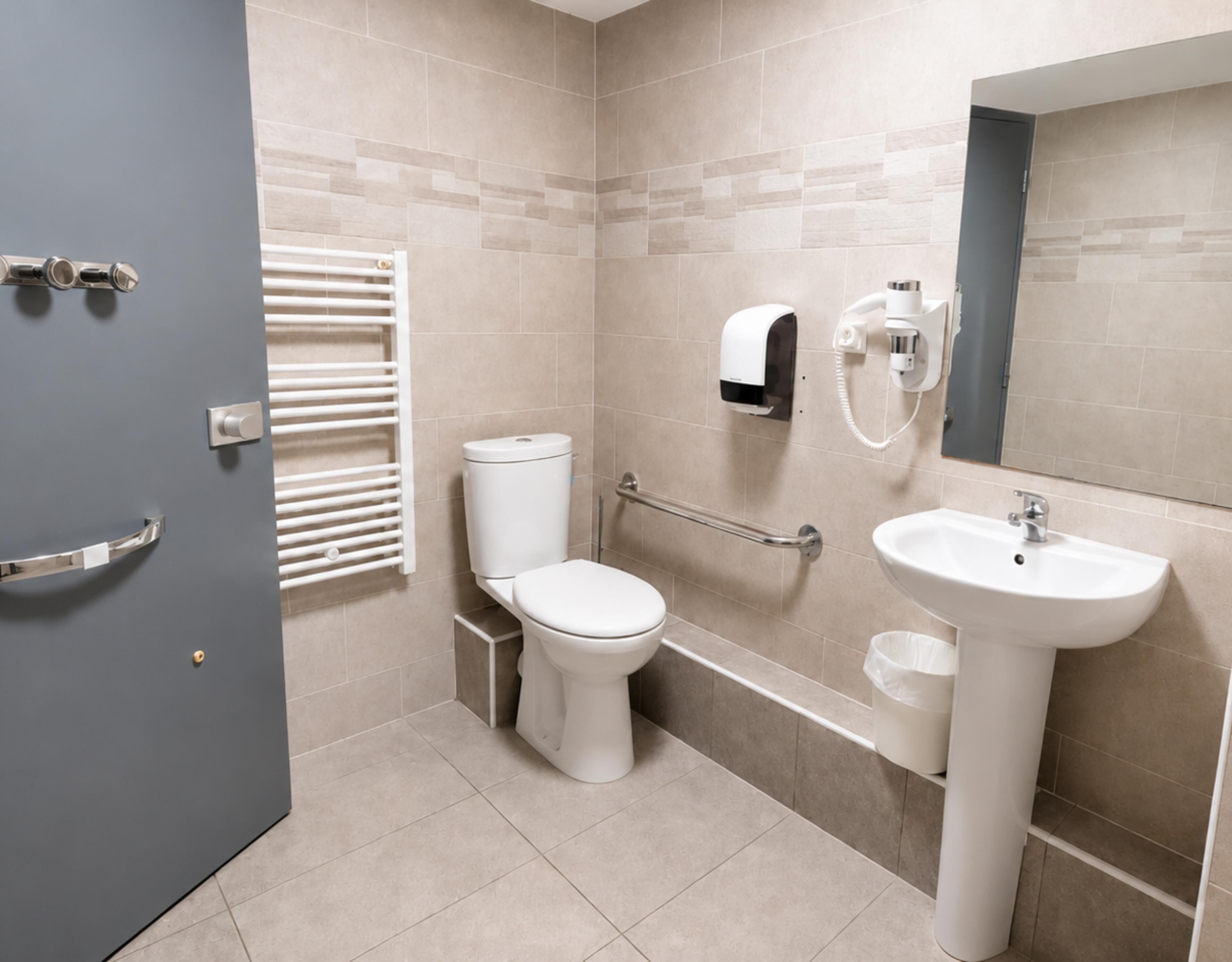 Une salle de bain équipée de toilettes, d’un lavabo, d’un porte-serviettes et d’un sèche-mains.