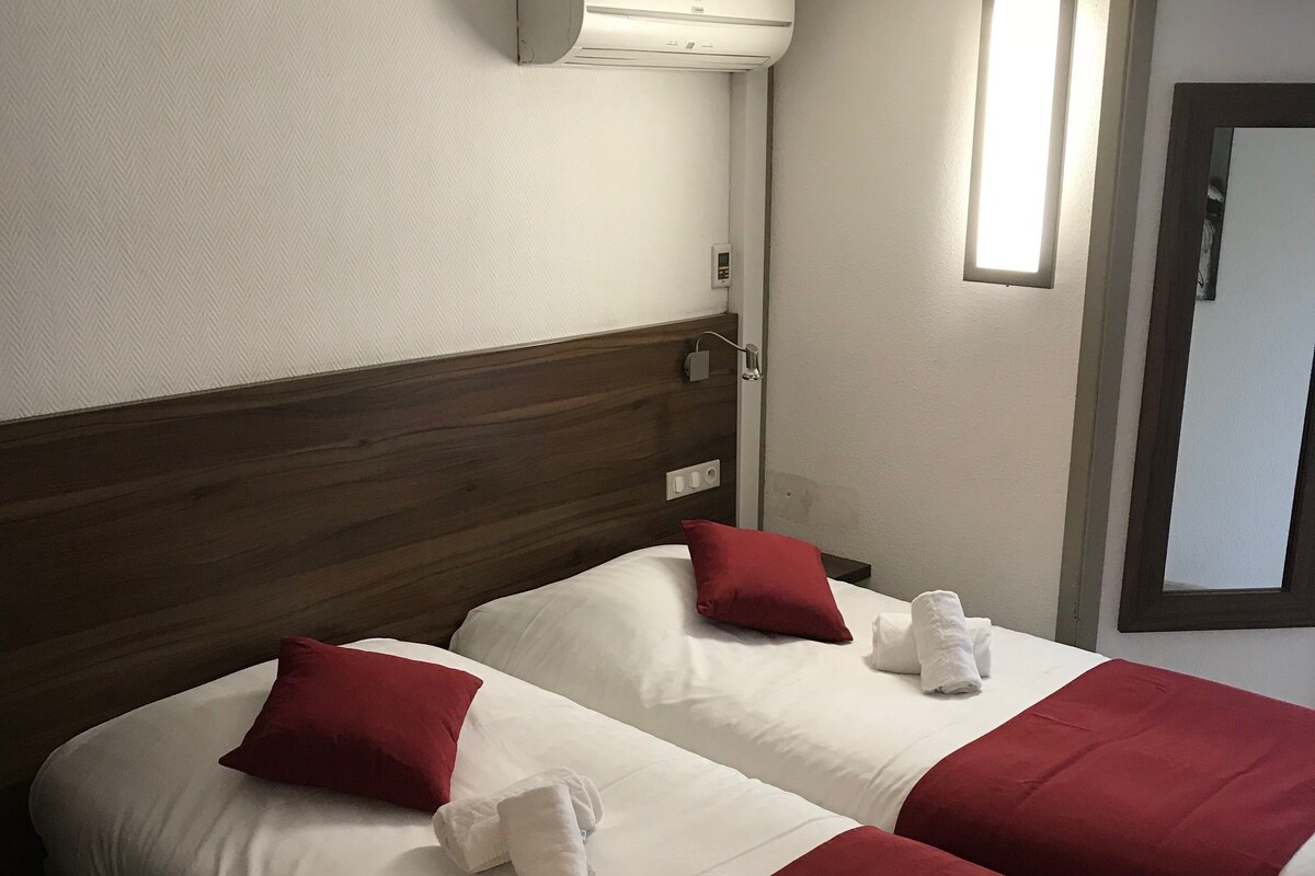 A hotel room with two beds, white bedding, red pillows, and a red blanket.