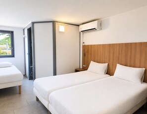 A hotel room with two beds, a wooden headboard, a window, and an air conditioning unit.