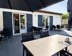 Un patio al aire libre con una mesa y sillas, una zona de estar techada y vistas al edificio contiguo.
