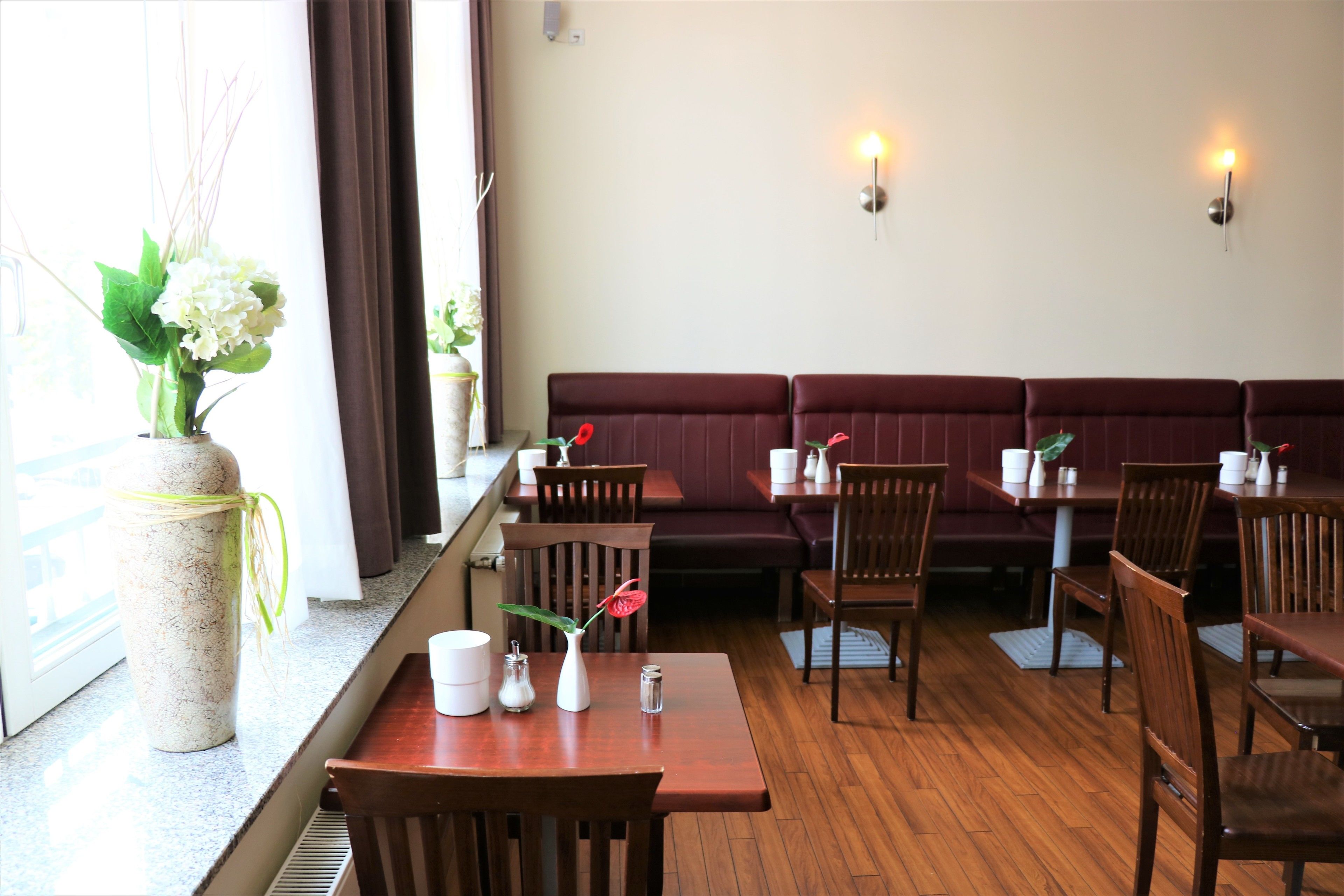 Un restaurant avec des tables et des chaises en bois, un vase rempli de fleurs sur le comptoir et un espace avec des bancs.