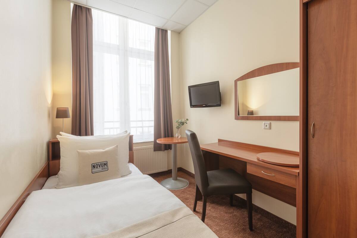 Une chambre d’hôtel avec un lit, un bureau, une chaise, une télévision et une fenêtre avec des rideaux.