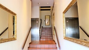 Eine Treppe mit roten Fliesen und einem Geländer, gesäumt von zwei großen Spiegeln mit aufwendigen Goldrahmen.