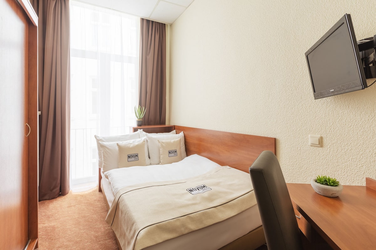Une chambre d’hôtel avec un lit, un bureau, une télévision et une fenêtre avec des rideaux.