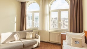 Ein Hotelzimmer mit einer Couch, einem Bett und großen Fenstern mit Blick auf die Stadt.