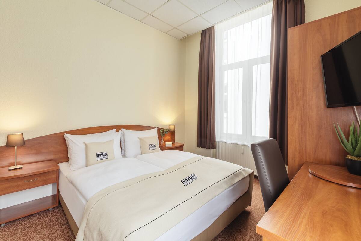 Une chambre d’hôtel comprenant un lit, des tables de chevet, un bureau, une chaise, une télévision et une fenêtre avec des rideaux.
