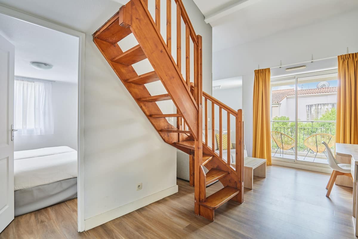 Un apartamento moderno con una escalera de madera, un balcón con cortinas amarillas y un comedor.