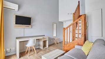 Een moderne woonkamer met een houten bureau, een grijze bank, een houten trap en een wandtelevisie.