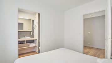 Een slaapkamer met een bed, een badkamer met een wastafel en spiegel, en een houten vloer.