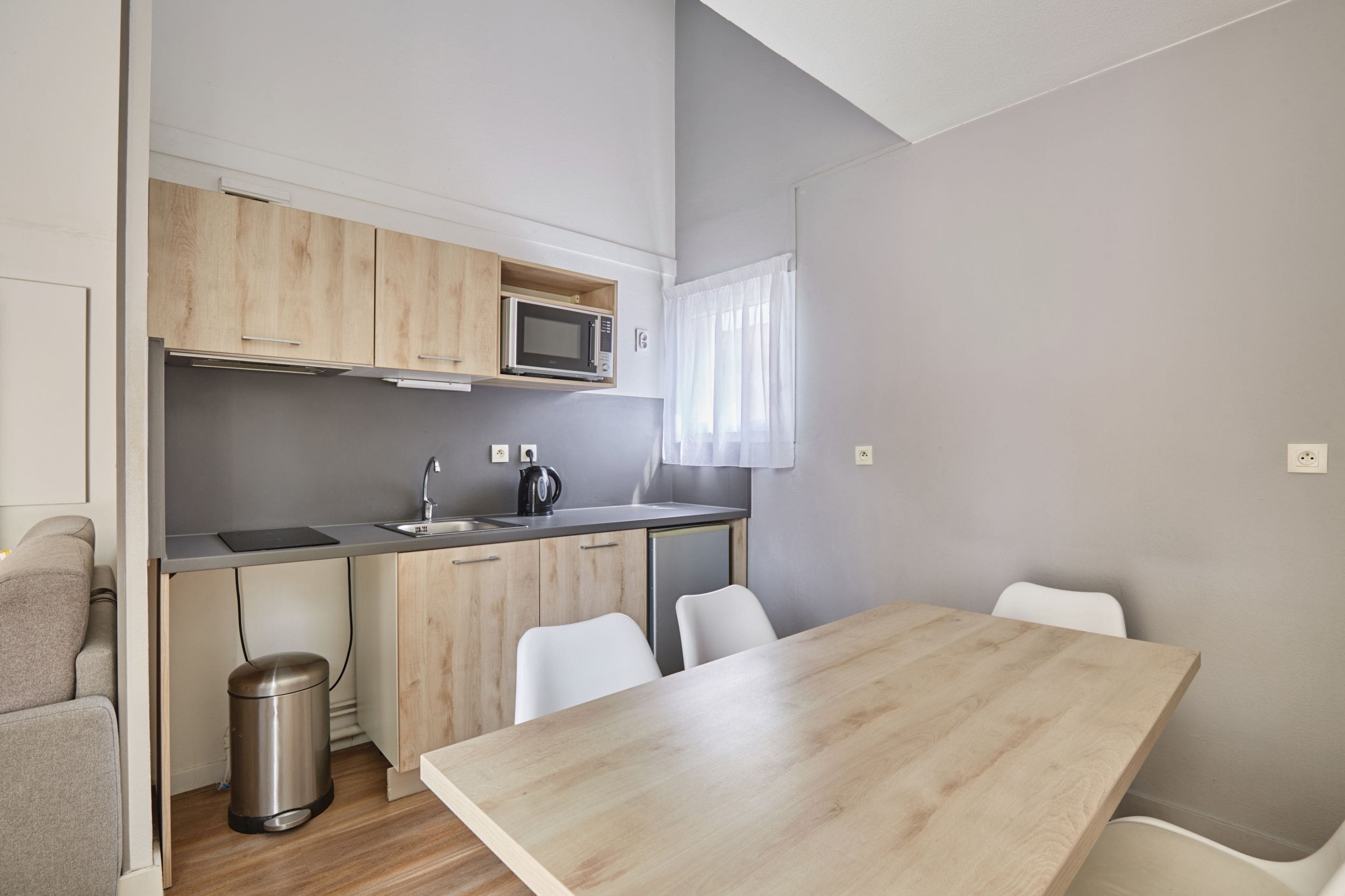 Una cocina compacta con microondas, lavamanos y sillas blancas.