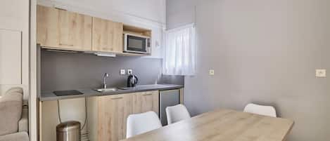 A compact kitchen with a microwave, sink, and white chairs.