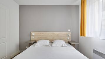Un dormitorio con una cama individual, cabecera de madera, dos mesitas de noche y un ventanal con cortinas amarillas.