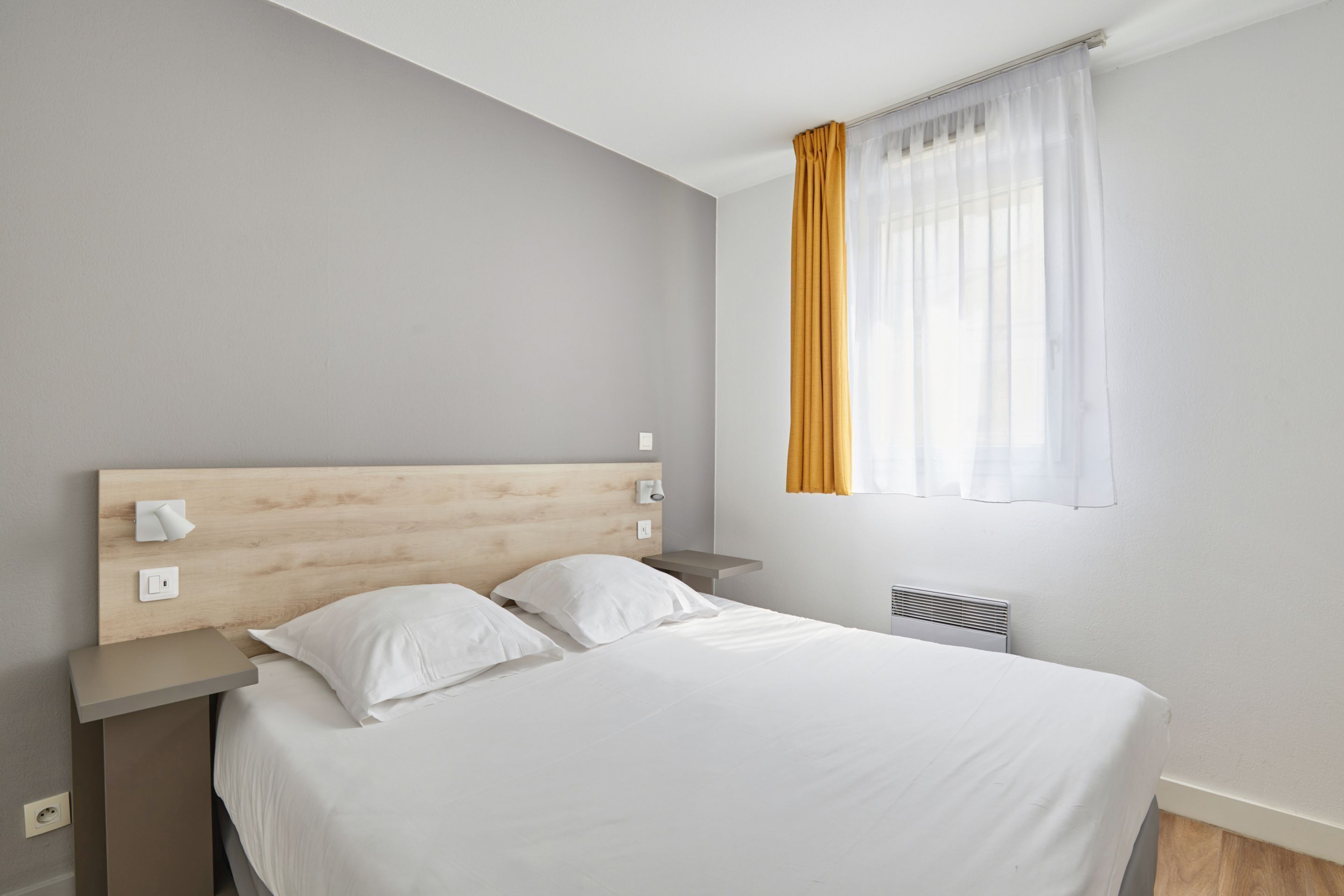 A neatly made bed with white linens, a wooden headboard, and a bedside table with a lamp.
