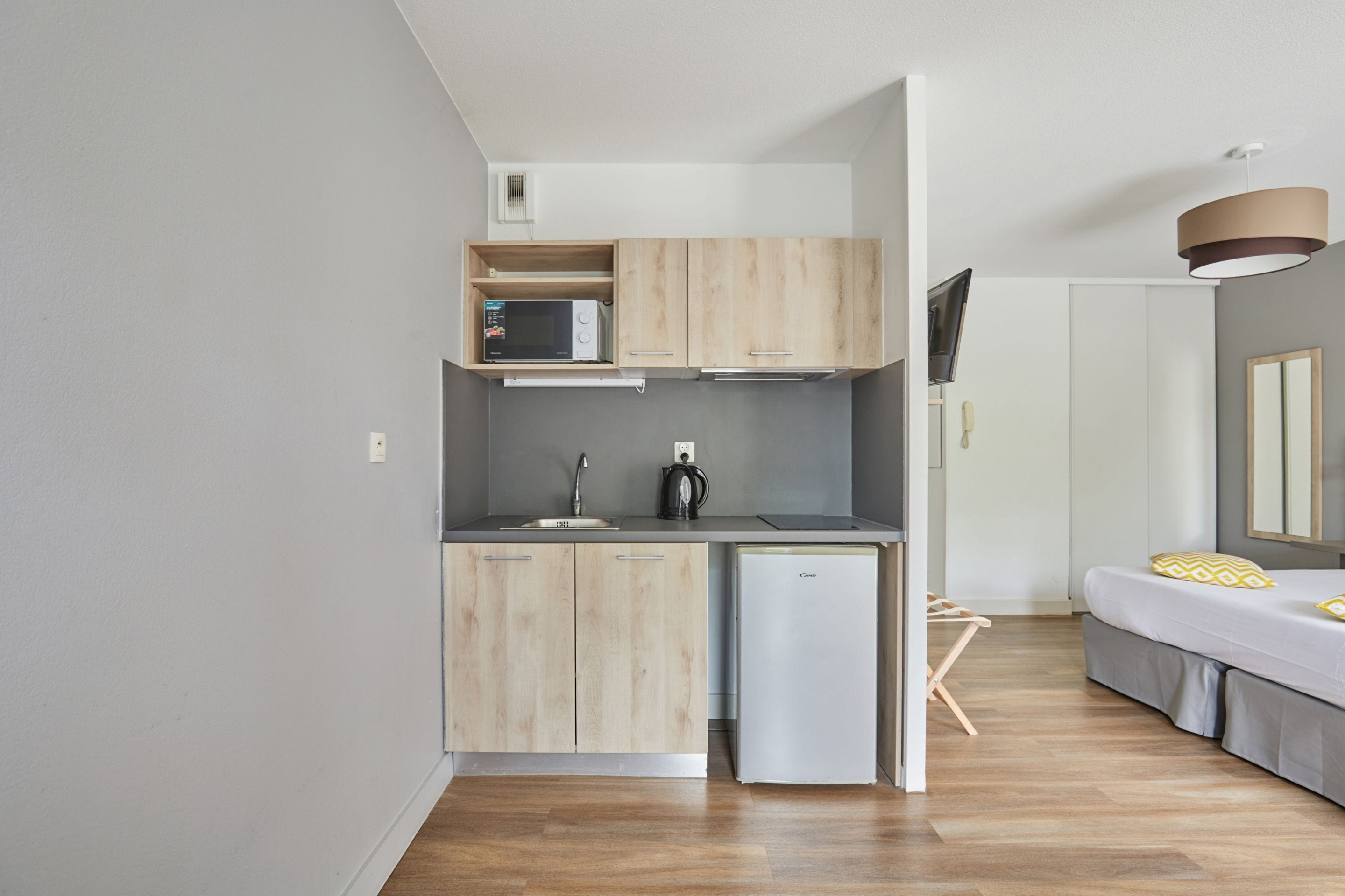 Una cocina compacta con microondas, lavamanos y un refrigerador pequeño.