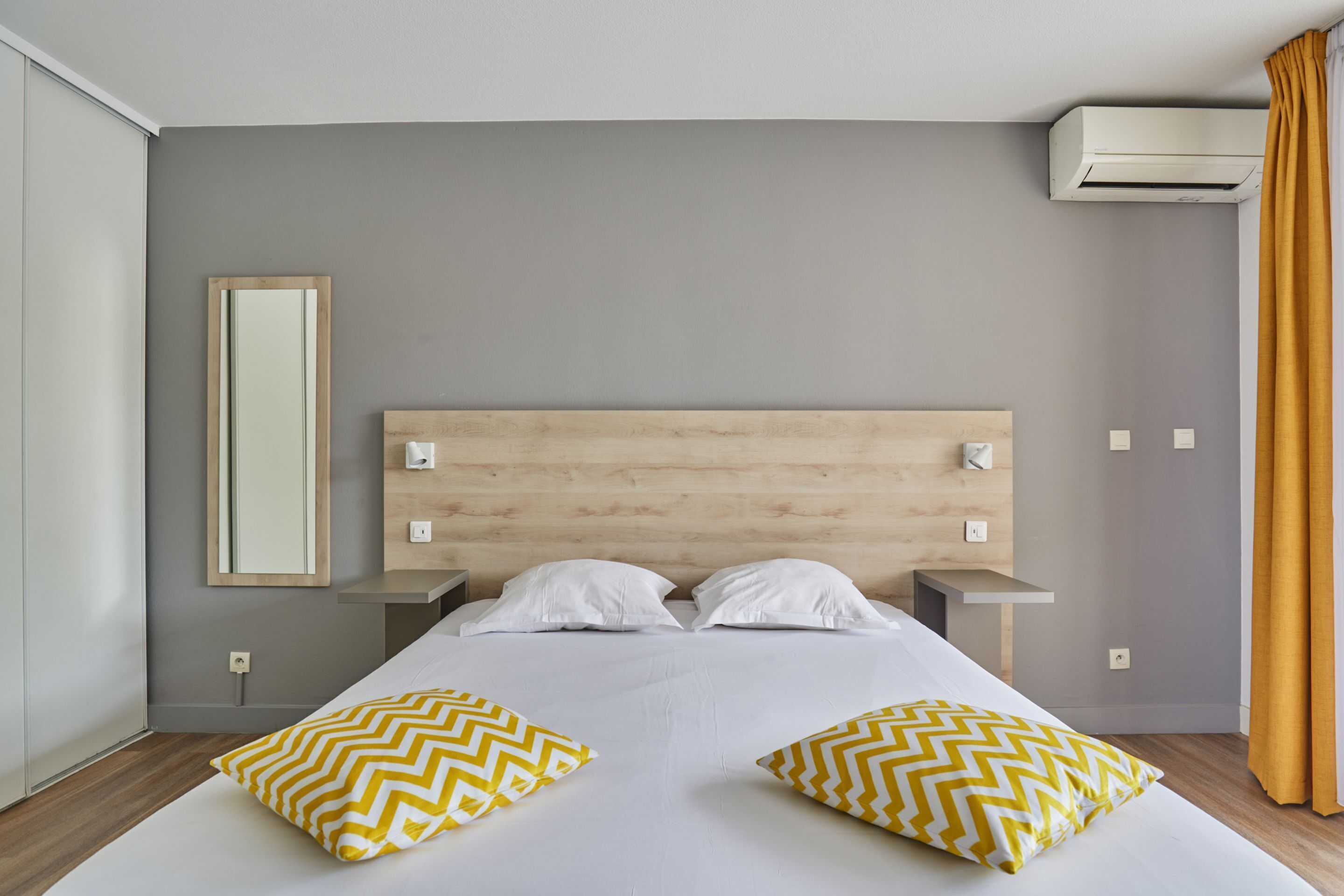 Et hotelværelse med en stor seng, to sengeborde, et spejl og en aircondition.