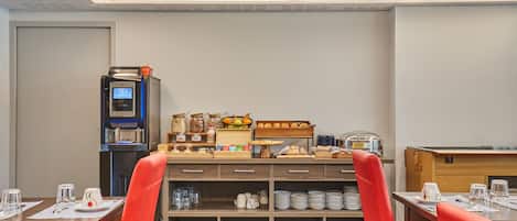 A hotel dining area with a buffet setup, a coffee machine, and seating arrangements.