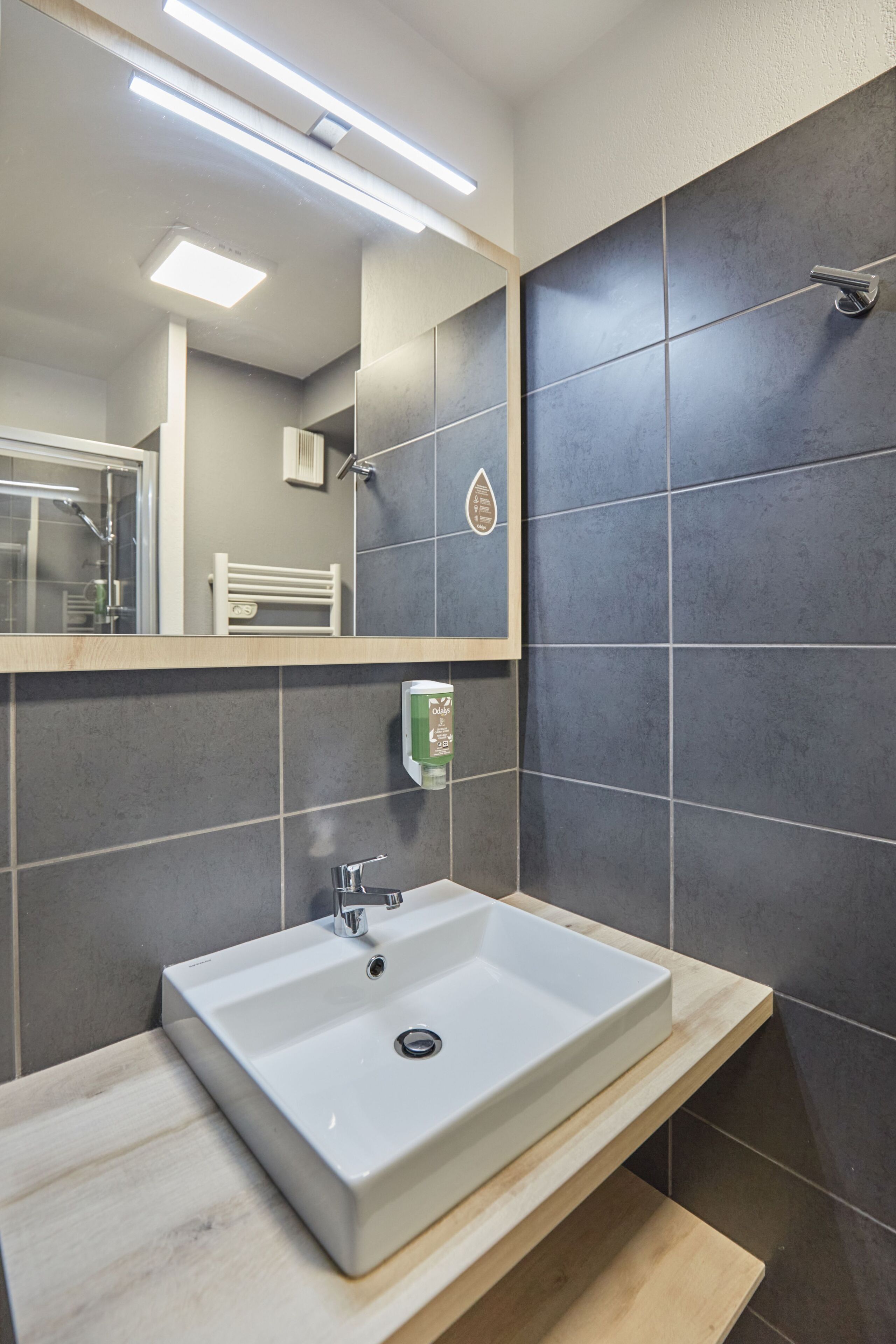 Un baño moderno con un lavabo rectangular, un espejo y un dispensador de jabón de mano.