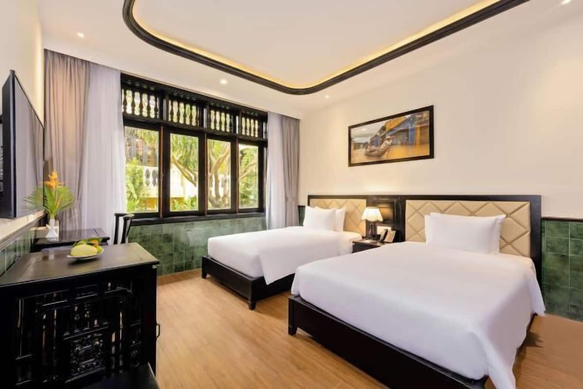 Ein Hotelzimmer mit zwei Betten, einem Schreibtisch, einem Stuhl, einem Fernseher und einem Fenster mit Vorhängen.