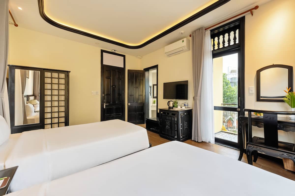 Ein Hotelzimmer mit zwei Betten, einem Fernseher, einem Schreibtisch mit Pflanze und einem Balkon mit Blick.