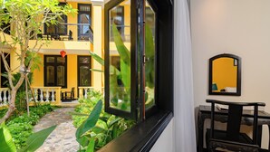 Une pièce avec vue sur un immeuble jaune, une fenêtre avec un rideau, une petite table avec une chaise et un miroir au mur.