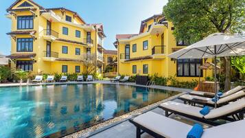 A pool area with lounge chairs and a building with balconies.
