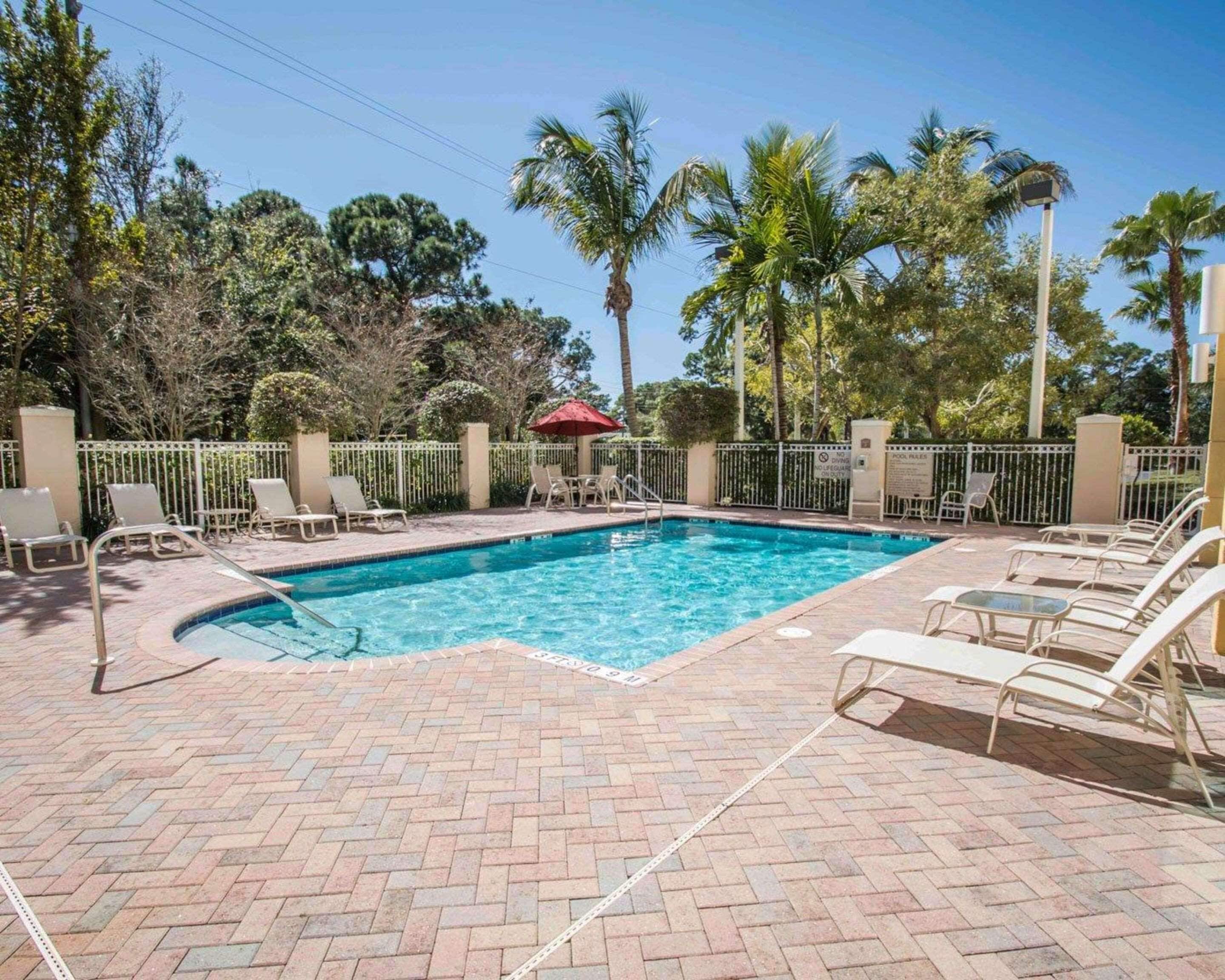 A rectangular swimming pool with a brick deck, surrounded by white metal railings and palm trees.