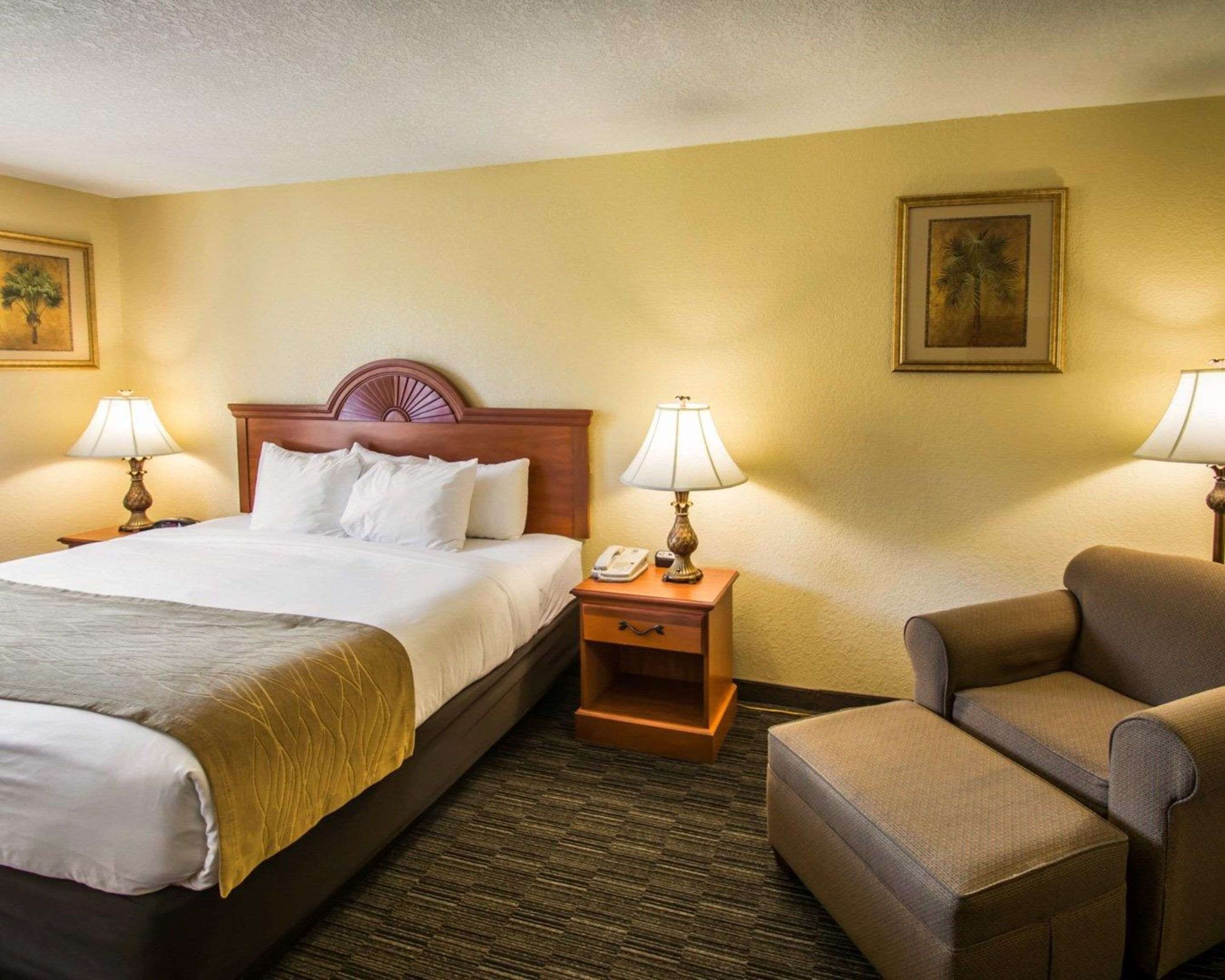 A hotel room with a large bed, two bedside tables with lamps, a chair, and a nightstand with a phone.