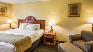 A hotel room with a large bed, two bedside tables with lamps, a chair, and a nightstand with a phone.
