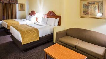 Een hotelkamer met twee bedden, een bank, een houten tafel en een kamerbreed tapijt met een patroon.