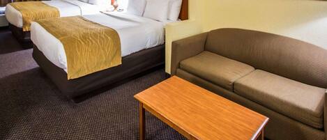 Una habitación de hotel con dos camas, un sofá, una mesa de madera y una alfombra estampada.