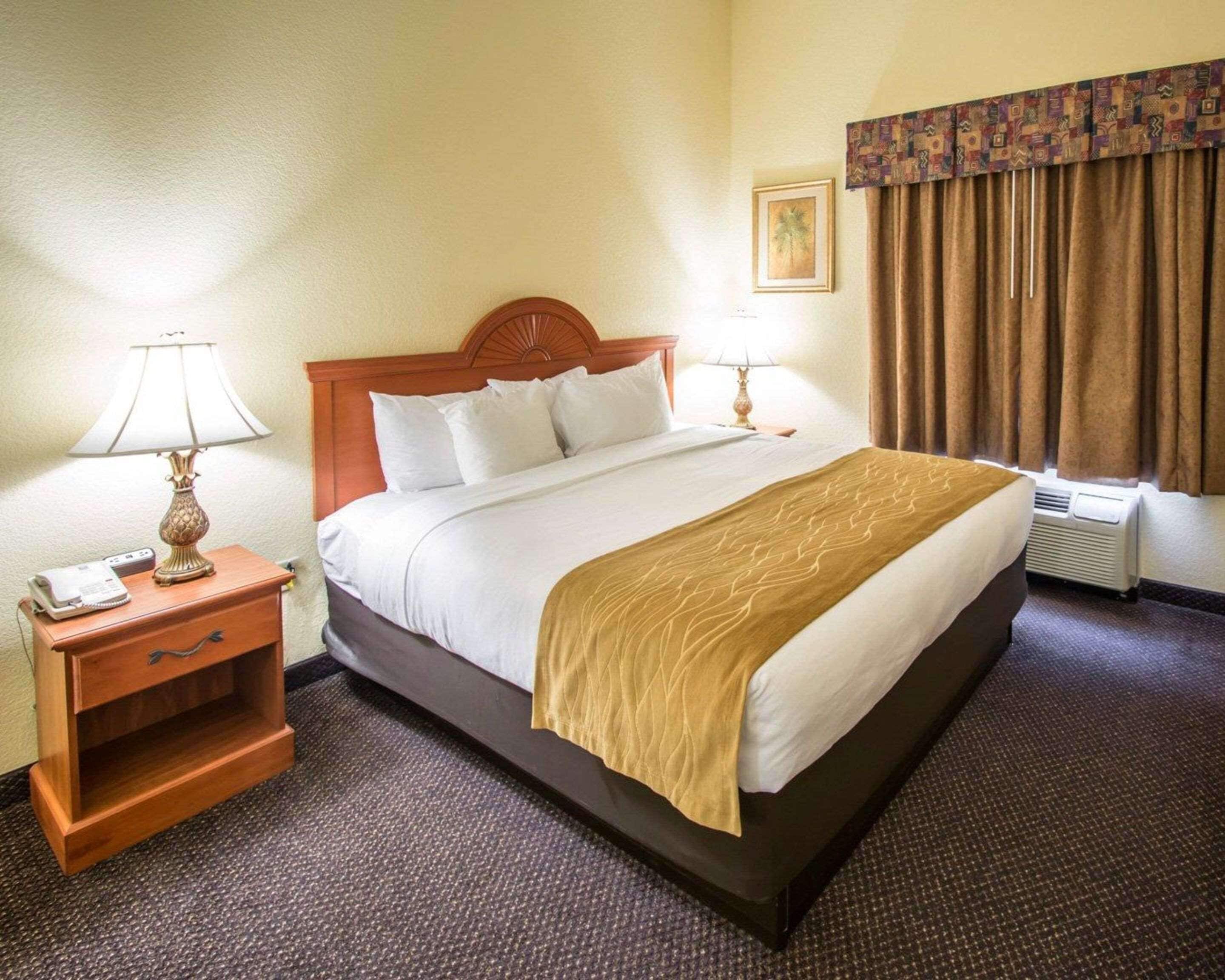 A hotel room with a large bed, two bedside tables with lamps, a heater, and a window with curtains.