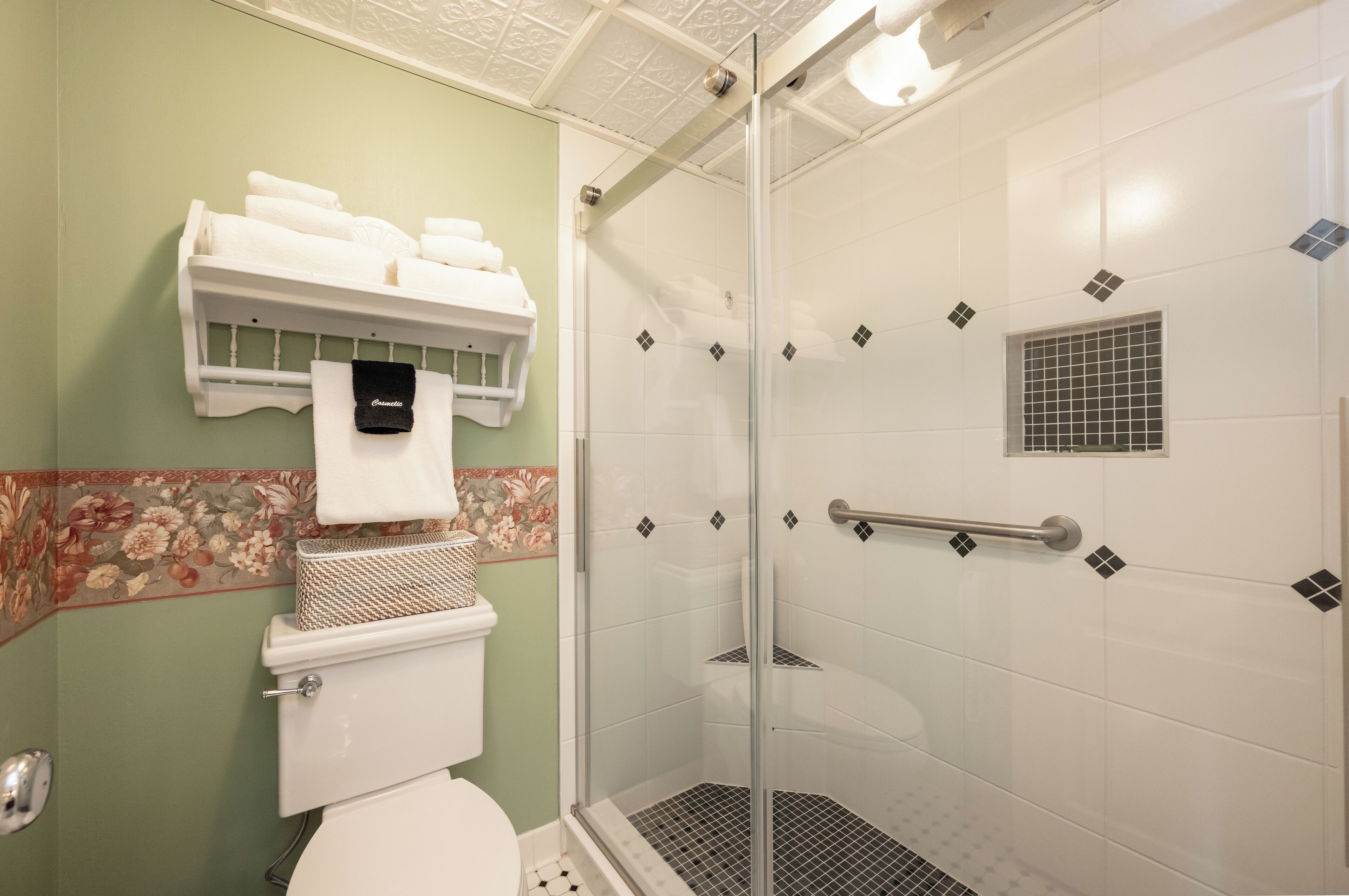A bathroom with a toilet, a shower with a glass door, and a towel rack with folded towels.