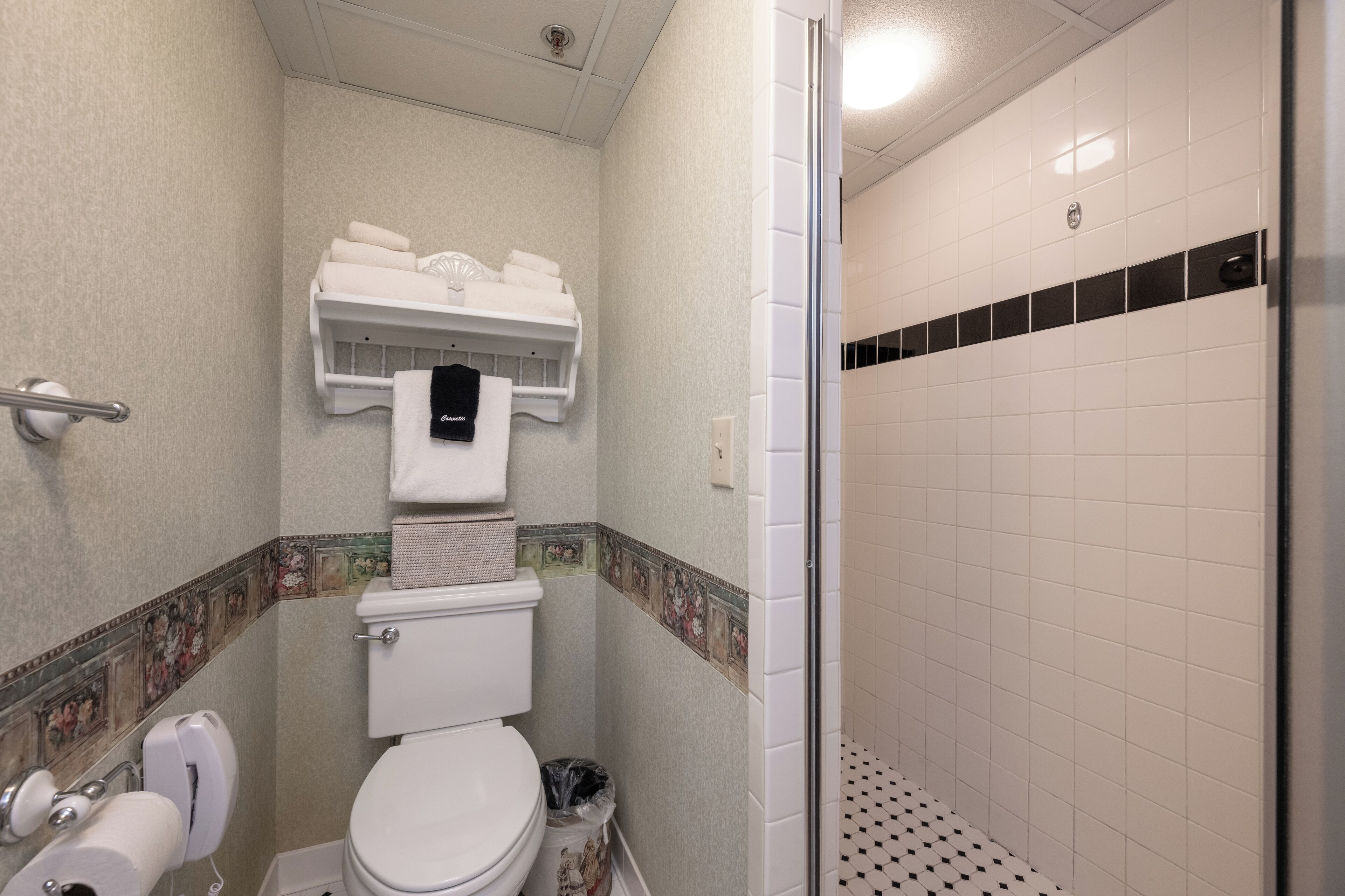 Egy mosdó, amelyben található egy WC, egy papírtörlő-adagoló és egy szemeteskosár.