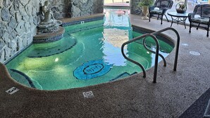 Un área de piscina interior con pared de piedra, una pequeña fuente y sillas de descanso.