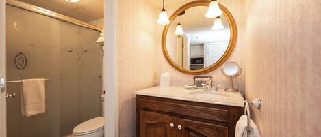 A bathroom with a shower, toilet, vanity with a mirror, and a towel rack.